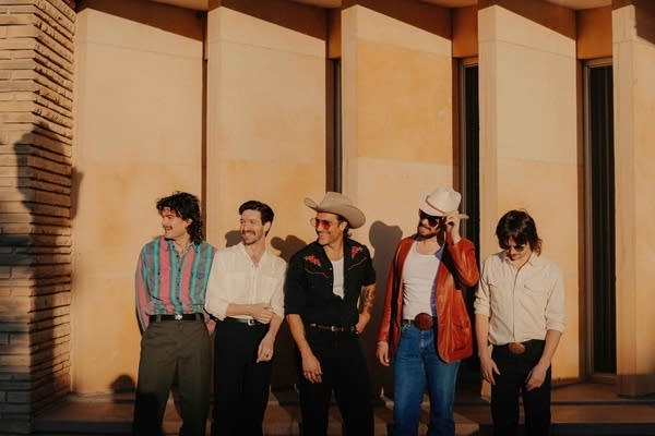 Five guys standing outside a building with vertical louvered stone slabs