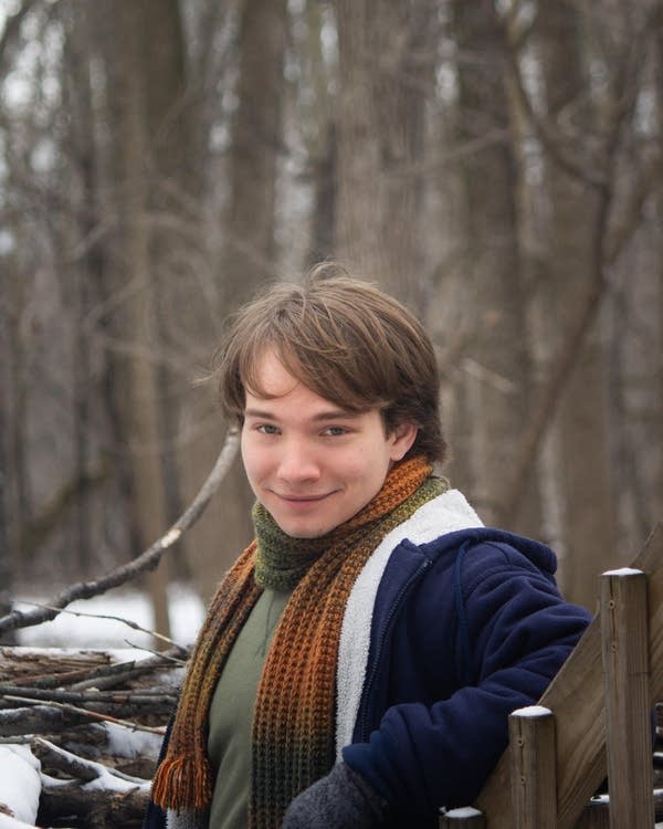 A man in winter clothing stands among trees in winter
