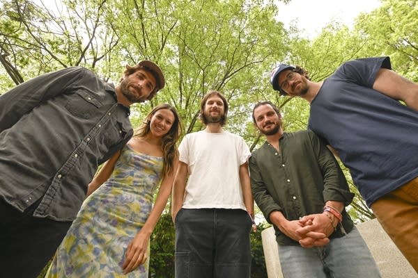 Five people gather in a semicircle under leafy trees for a low-angle group portrait
