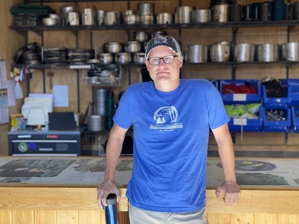 A man leans on a counter with camping equipment behind him.