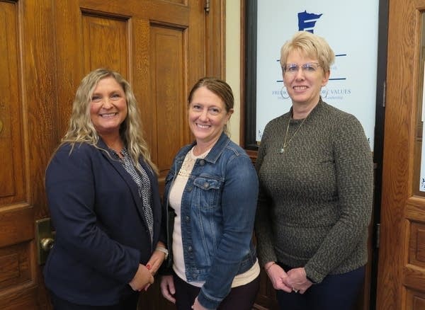 Three women stand in front of a door