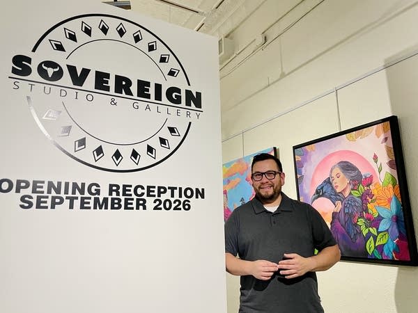 A man poses for a photo next to the sign for Sovereign Studio & Gallery.