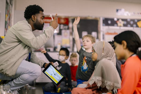 a man squatted down teaching elementary students
