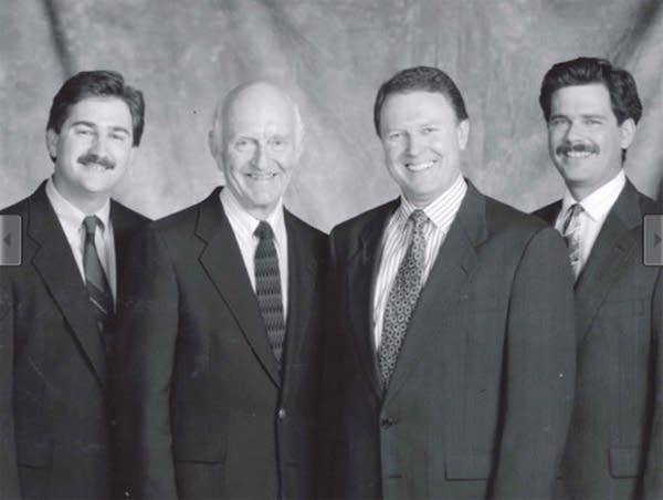 A black and white photo of four men in suits posing for a portrait.