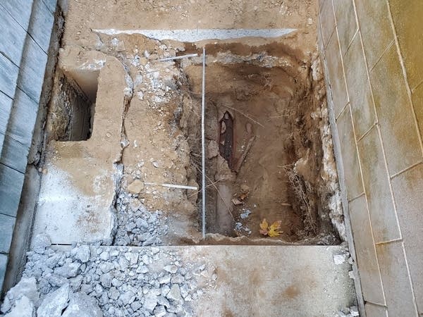 A 4 foot square hole cut into concrete exposing a busted clay pipe