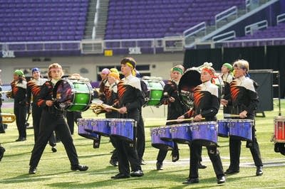 A marching band performs on the field of a football stadium.