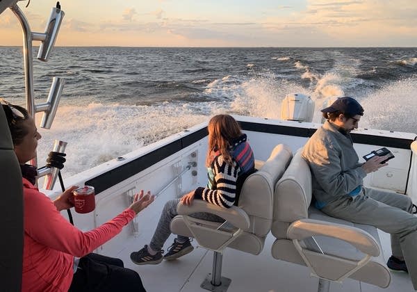 Three people sitting in the back of a boat. 