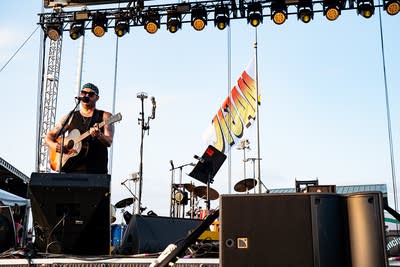 A musician sings and plays guitar on an outdoor stage