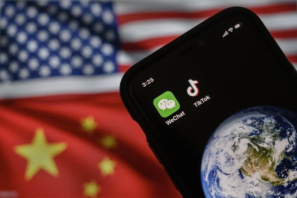 A mobile phone displaying the logos for Chinese apps WeChat and TikTok in front of a monitor showing the flags of the United States and China on an internet page.