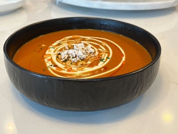 A bowl of orange bisque drizzled with cream and garnished with popped sorghum.