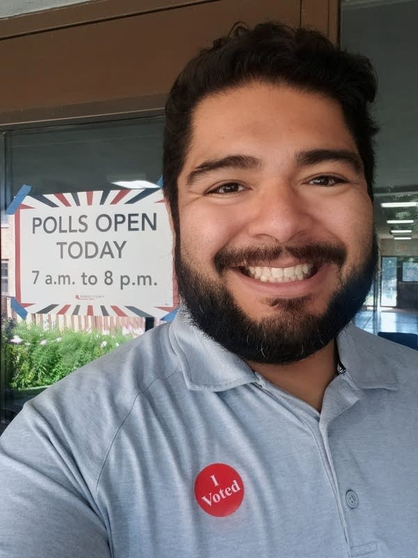 A man poses outside of a building with a sign saying "Polls Open Today."