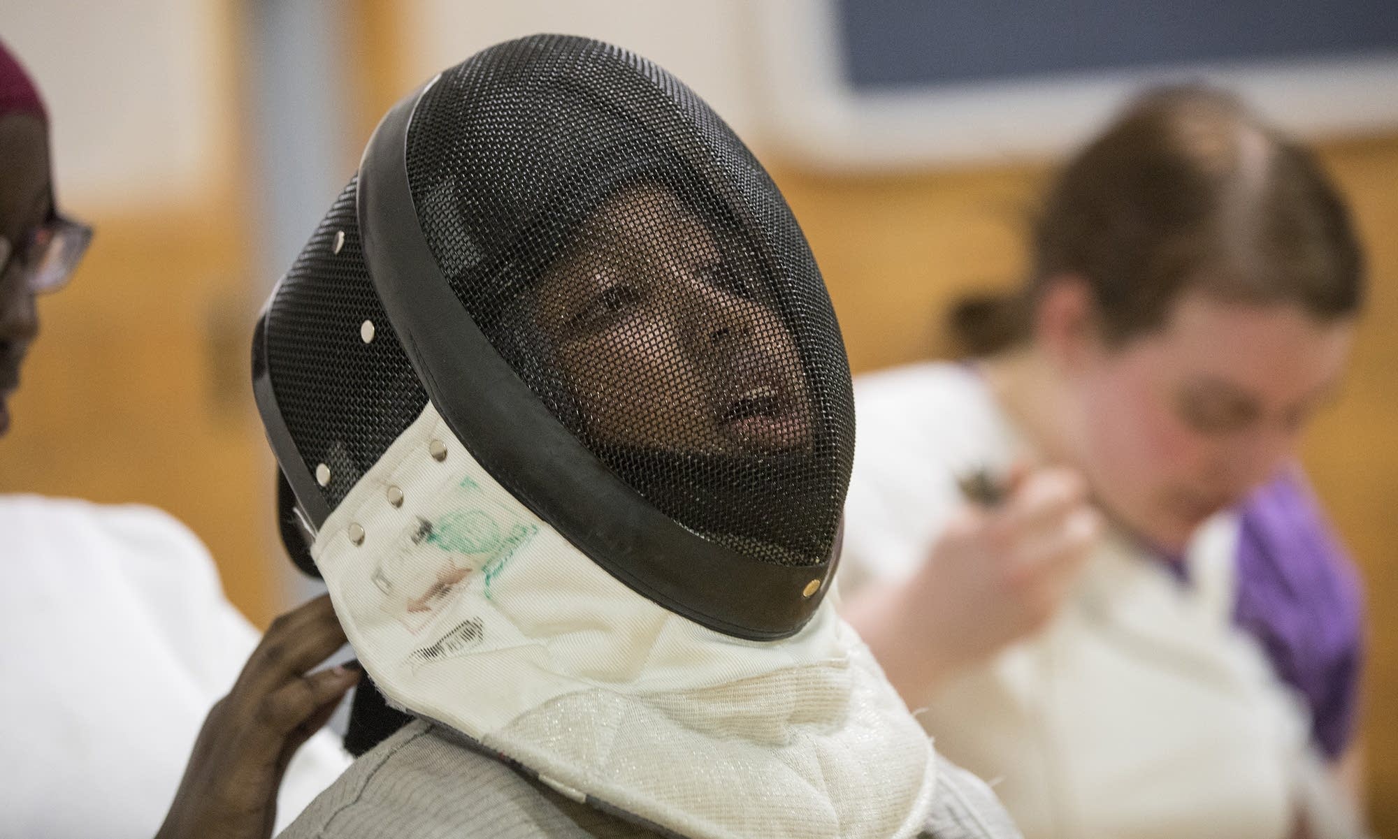 Saara Abdullahi gets help adjusting her fencing mask.