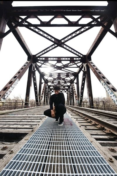 A man kneels down on a mixed-use (auto, pedestrian, railway) bridge