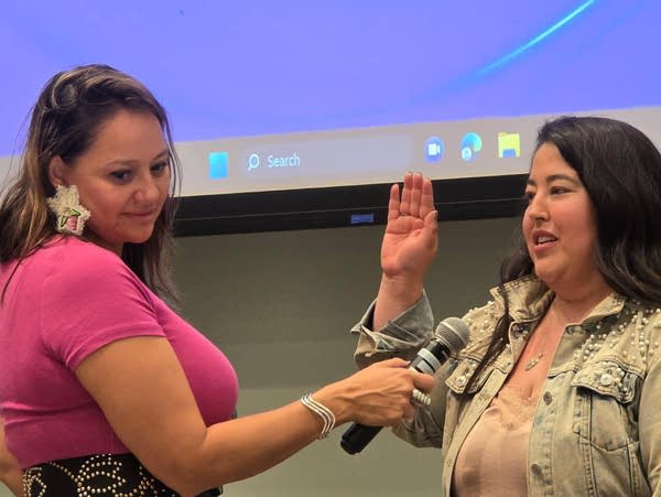 A woman holds her hand up and speaks into a microphone.