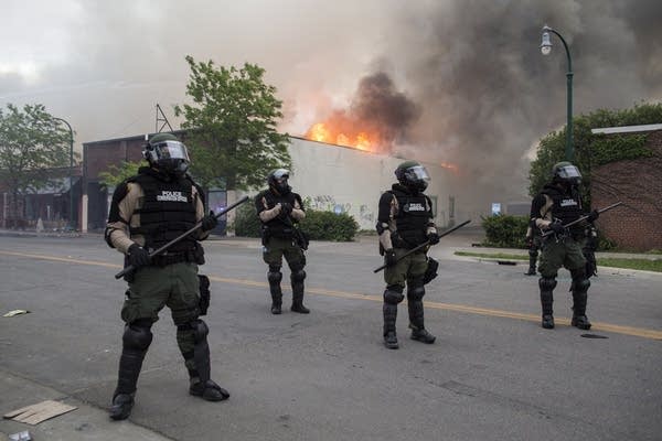 State patrol stand in front of burning buildings. 