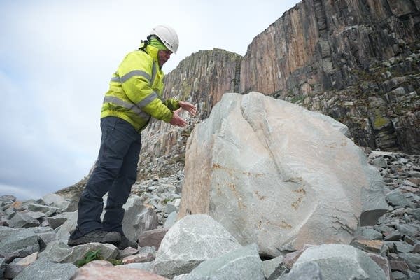 A man in a hi-vis vest and hardhat looks at a boulder of granite.