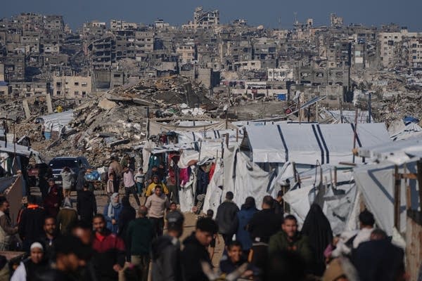 People walk past a tent camp.