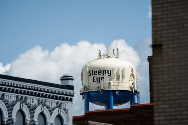 A water tower that reads "Sleepy Eye" stands over a small town. 