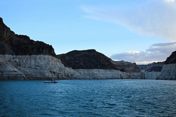 A boat navigates waters at sunset near the exposed upstream face of the Hoover Dam and the "bathtub ring", a white band of mineral deposits showing previous water levels, of Lake Mead on June 28, 2022 on Lake Mead along the Colorado River in Boulder City, Nevada. Millions of gallons of Colorado River hurtle through the Hoover Dam every day, generating electricity for hundreds of thousands of homes. But the mega drought desiccating the western United States is sending reservoir levels plummeting towards deadpool -- the point at which the dam can no longer produce power. (Photo by Patrick T. FALLON / AFP) (Photo by PATRICK T. FALLON/AFP via Getty Images)