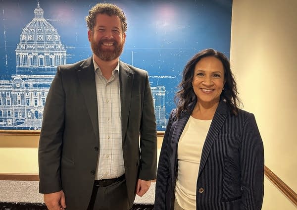 Two people smile for a pose in the press room of the capitol.