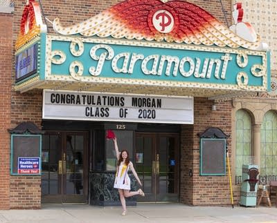 Person in a white dress poses under a theater marquee. 