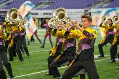 A marching band performs on the field of a football stadium.