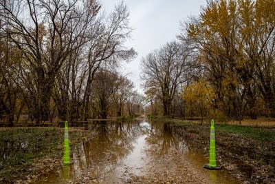 Two cones sit on the side of a road covered in water.