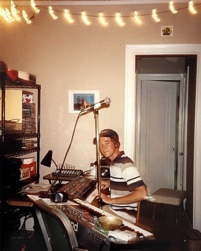 A man sits behind a console with keyboards.