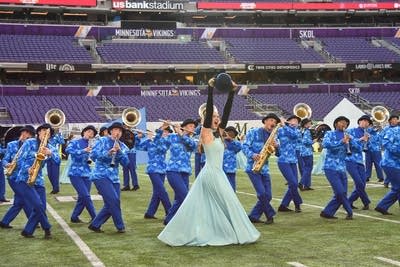 A marching band performs on the field of a football stadium.