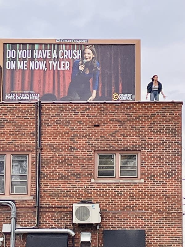 A person poses for a photo with a billboard