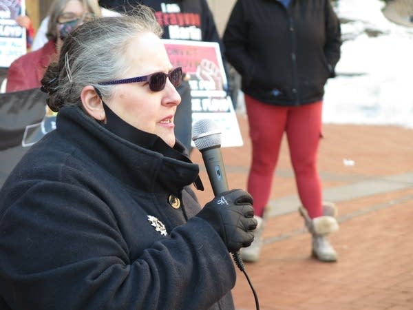 A woman wearing sunglasses speaks through a mic.