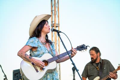 A musician sings and plays guitar on an outdoor stage