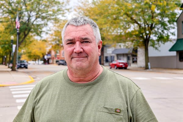 A man in a green shirt poses for a photo on a city street corner.