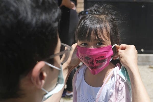 A father helps his daughter wear a mask. 