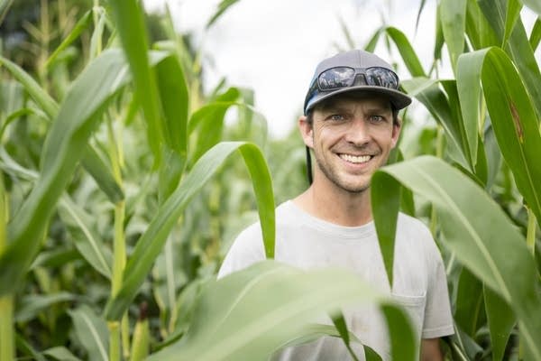A man stands in a cornfield, leaves partially obscure his torso