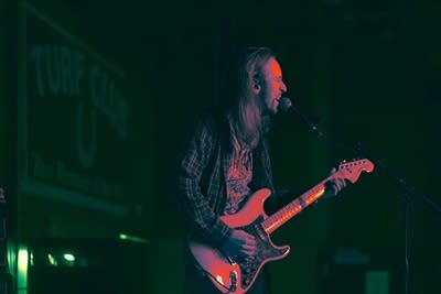A man sings and plays guitar onstage in a music venue
