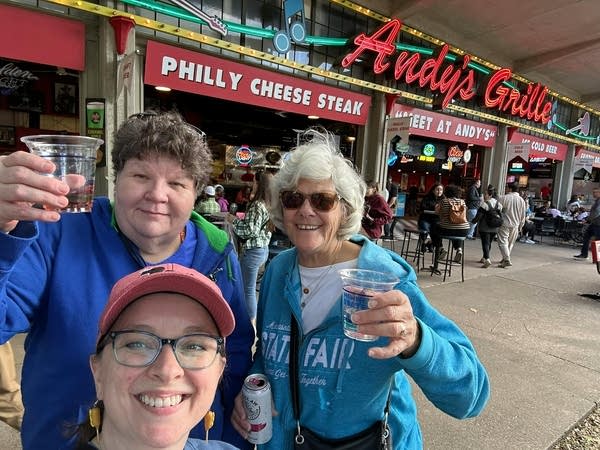 Three women smile for a photo with drinks