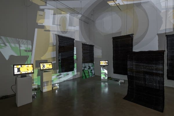 Room with computer screens, projected abstract images and hanging quilts