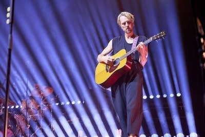 A musician plays guitar onstage in a large music venue