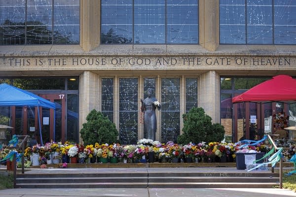 Wide shot of the Annunciation Catholic Church exterior. Many flower bouquets are placed in front of a bronze statue.