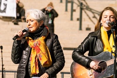 Two musicians perform together on an outdoor stage at a large rally