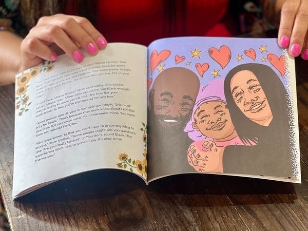 A woman holds open a children's book. The left page has text, and the right has a smiling family with hearts around their heads.