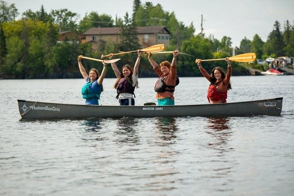 Four people raise their canoe paddles in canoe