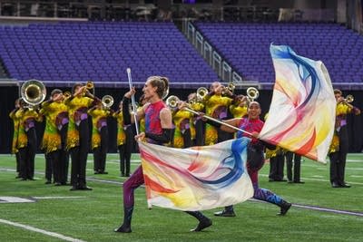 A marching band performs on the field of a football stadium.