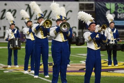 A marching band performs on the field of a football stadium.