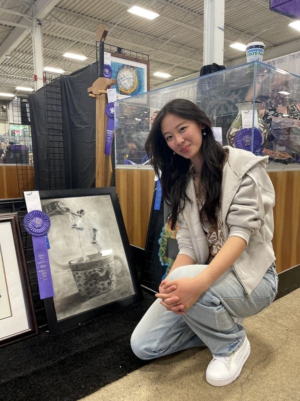 A woman kneels next to a charcoal drawing of two kids jumping into a teapot