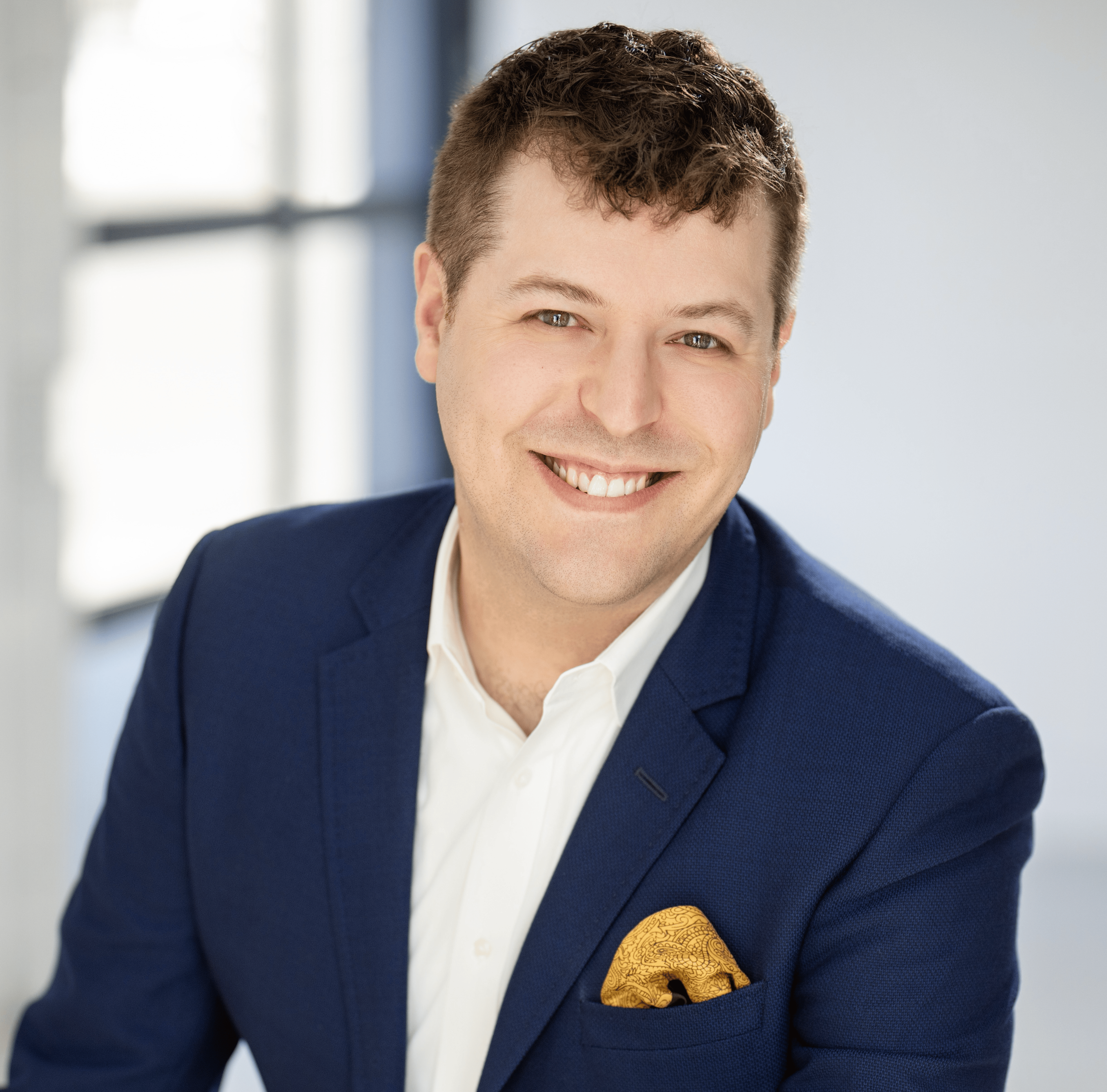 A man in a blue blazer and gold pocket square poses for a photo.