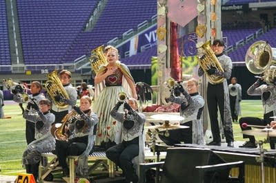 A marching band performs on the field of a football stadium.
