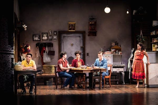 People sit in a kitchen setting on a stage.