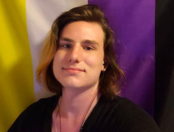 A person poses in front of yellow, white and purple stripes.